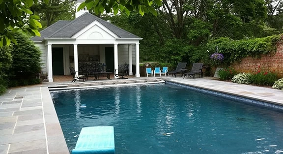 Custom gunite swimming pool in a Suffolk County backyard with elegant design, water features, and stone decking