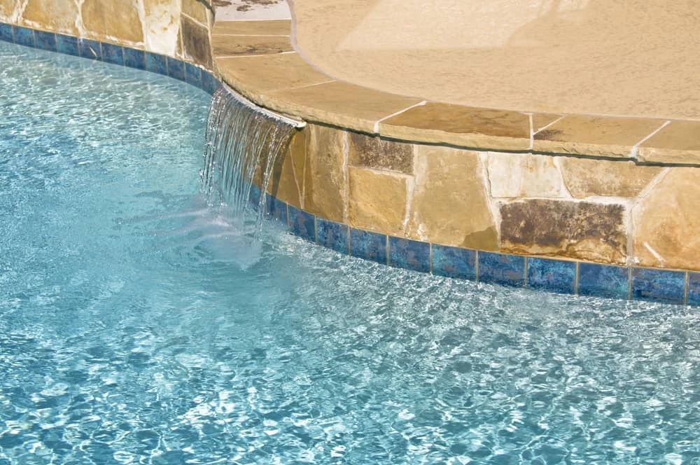 Side of a custom pool with a built-in bubbler creating gentle water movement in the shallow area, surrounded by stone coping and clear blue water