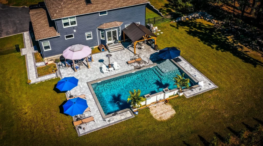 Aerial view of a landscaped backyard featuring a custom inground pool, patio area, and surrounding greenery, showcasing full outdoor design and layout