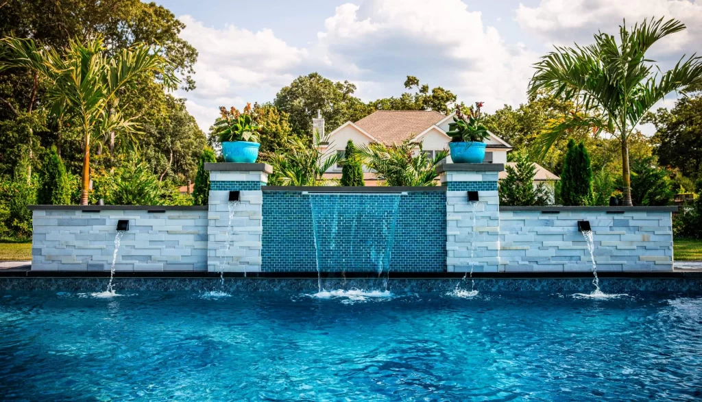 Inground swimming pool with a cascading stone waterfall and integrated water feature, surrounded by lush landscaping in a luxurious backyard setting