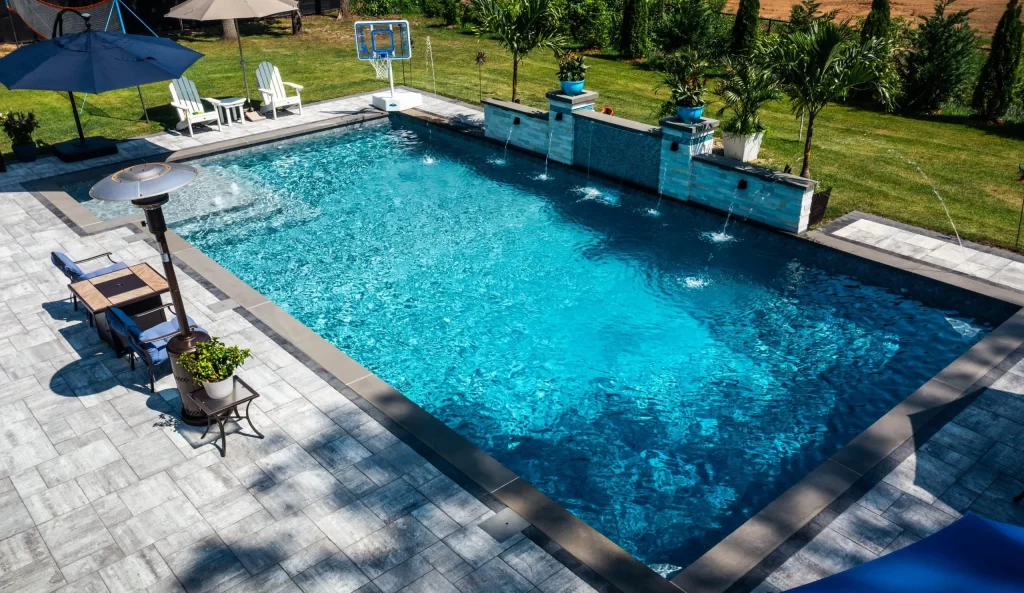 Custom swimming pool with a vibrant blue tiled floor and a matching blue umbrella providing shade over the poolside area, set in a landscaped backyard