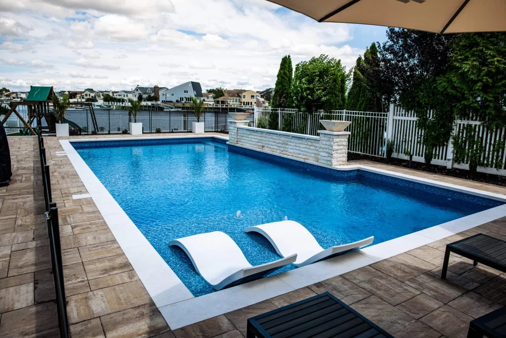 A pool with two lounge chairs and an umbrella.