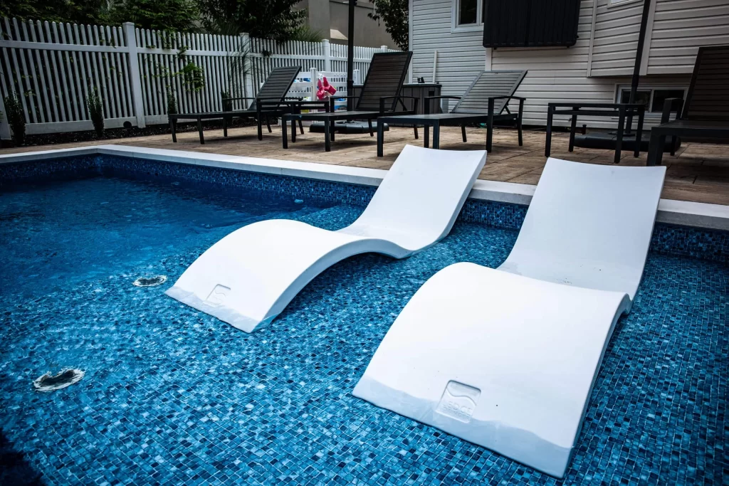 Swimming pool with a natural stone wall feature and a surrounding patio area with lounge seating, creating a luxurious and functional backyard environment