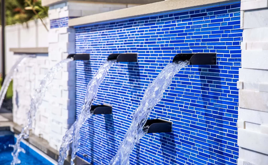 Blue mosaic pool wall with water spouts.