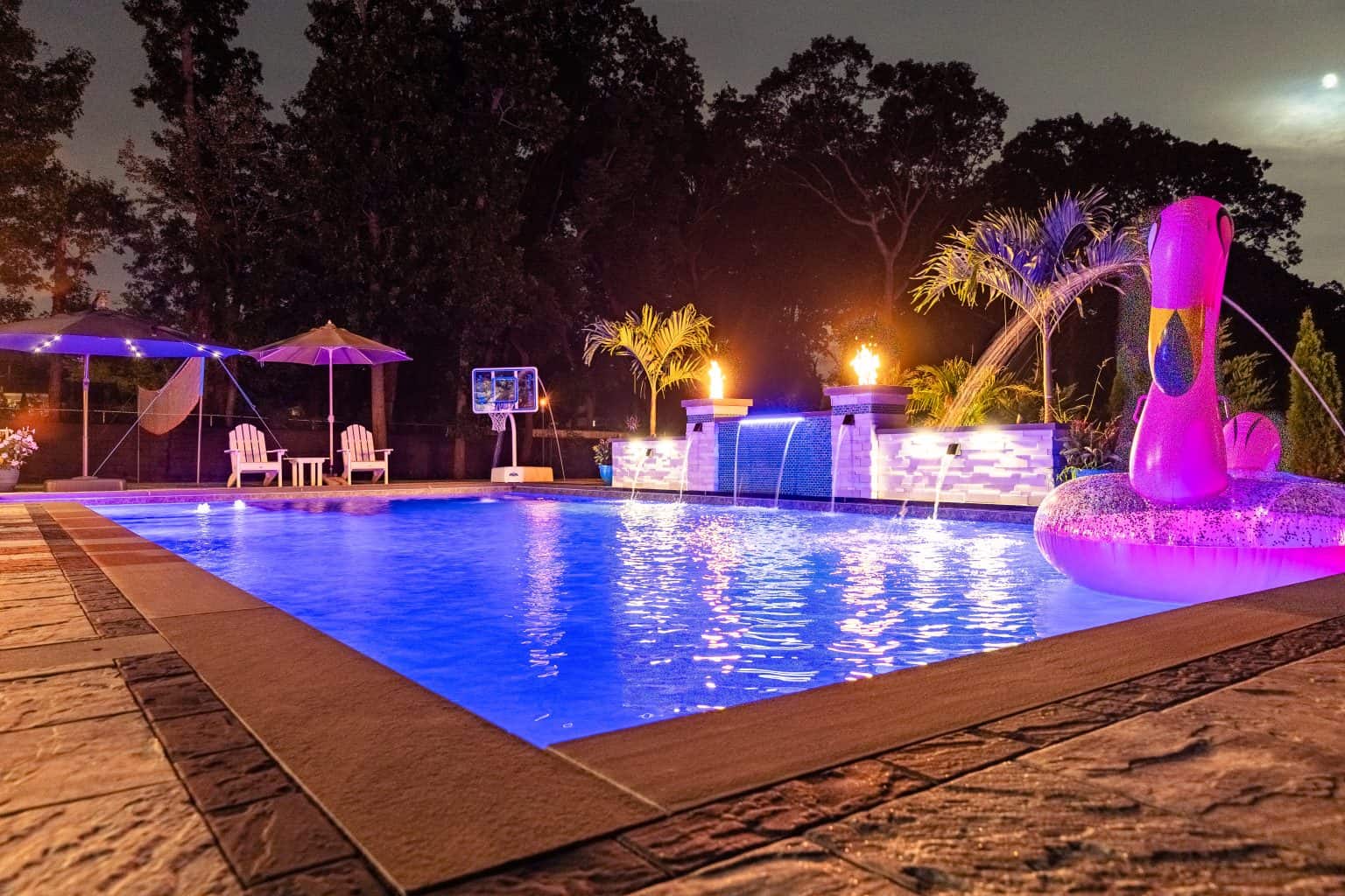 pool and backyard at dusk with ambient lighting and flamingo pool float.