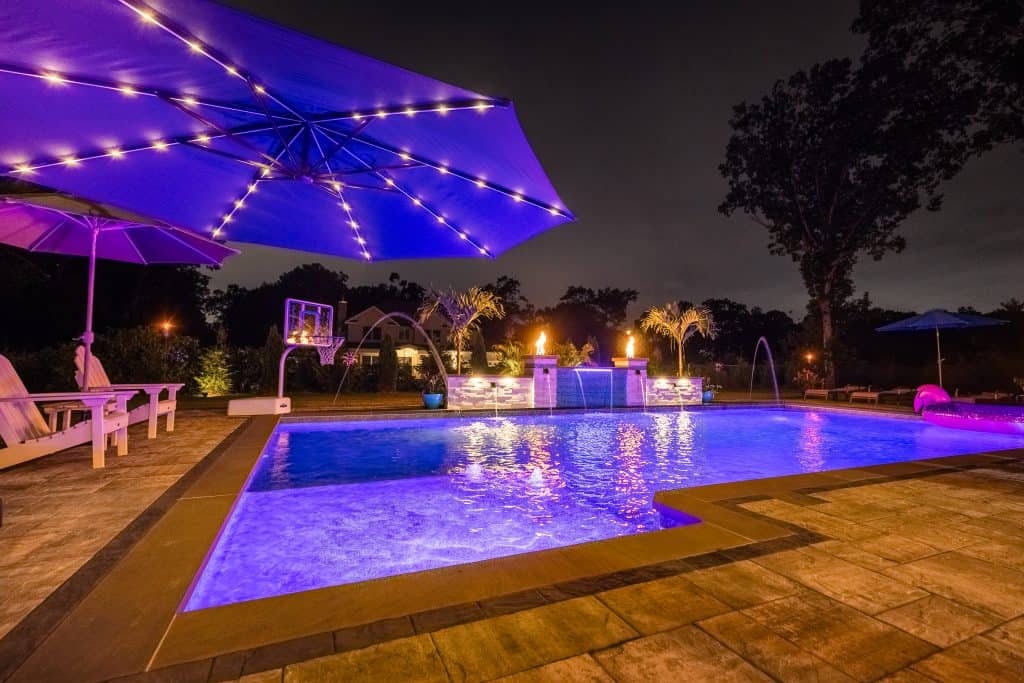 inground pool in yard at night with blue pool lighting.