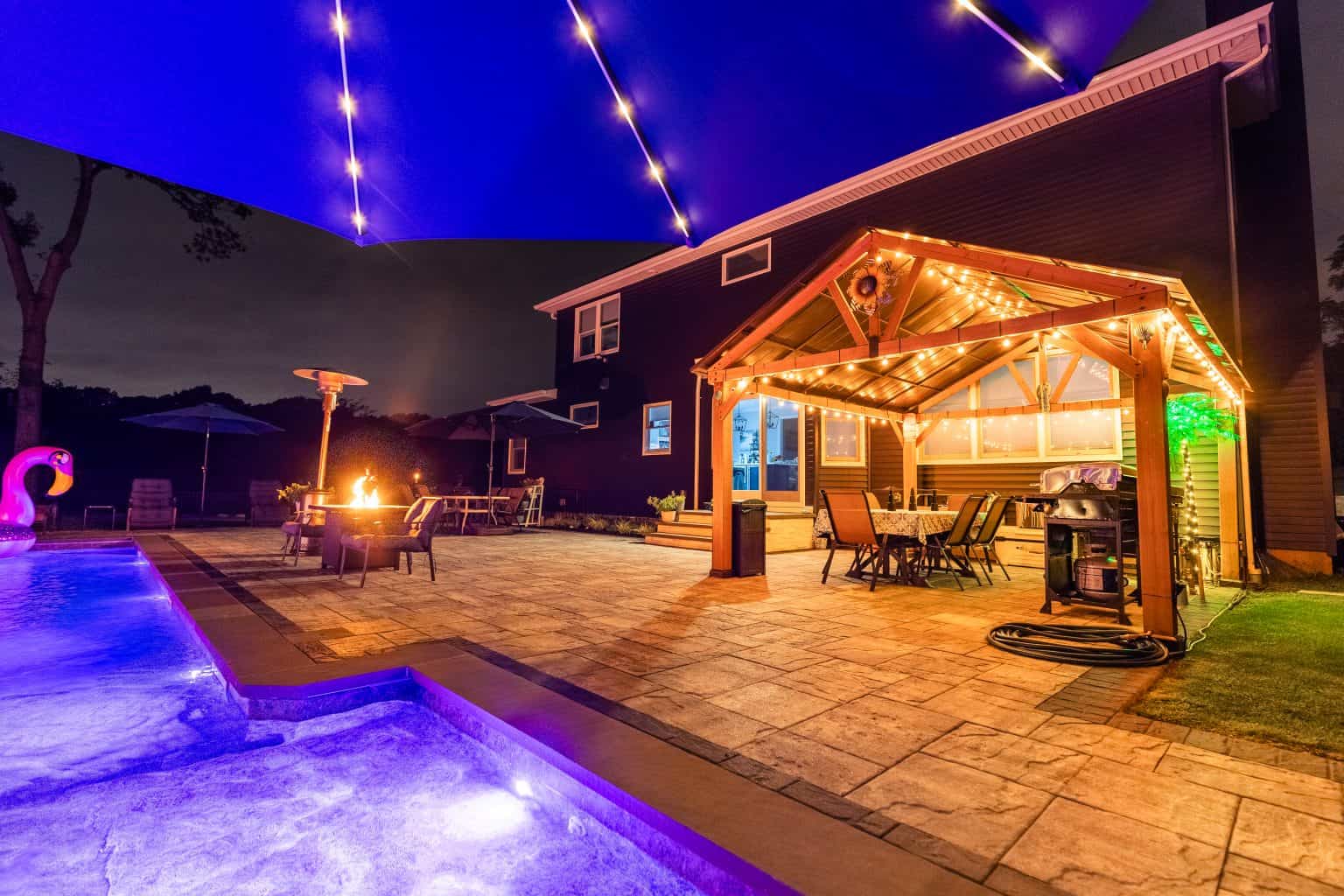 yard at night with led pool lighting and a pergola.