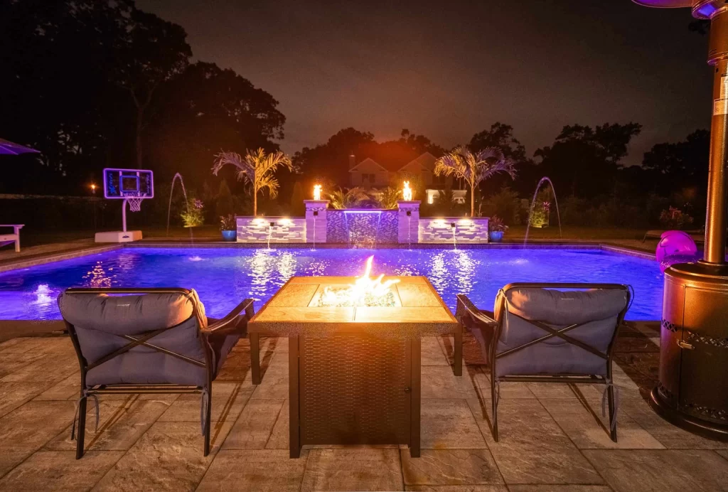 Swimming pool with a fire pit and surrounding chairs, creating a cozy outdoor gathering space blending luxury pool design with custom fire features and patio seating