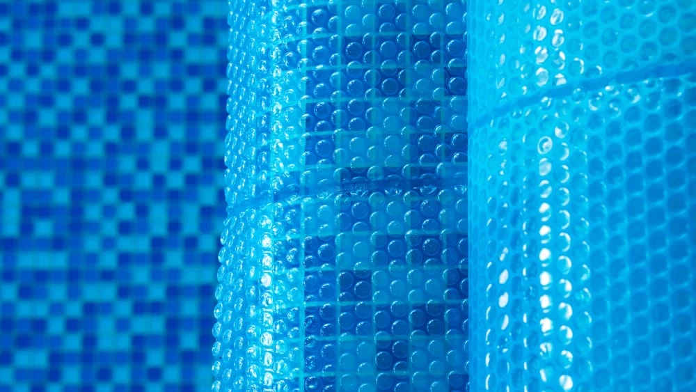Close-up of blue bubble wrap pool covers, with a mosaic-tiled pool wall in the background—a textured, blue-toned pattern that showcases the quality finish you can expect from a professional inground pool installation.