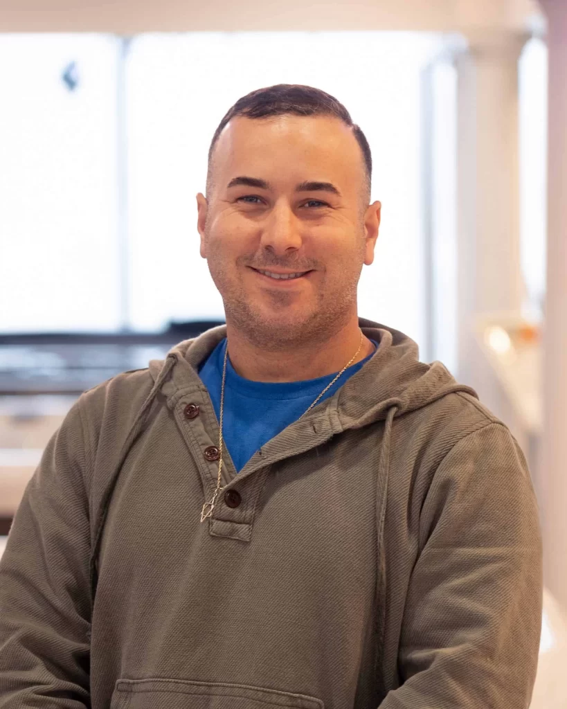 Jesse Schreier, founder of a Long Island pool company, standing confidently on-site near a custom pool project, wearing a polo shirt and smiling—representing trusted pool installation and outdoor living expertise